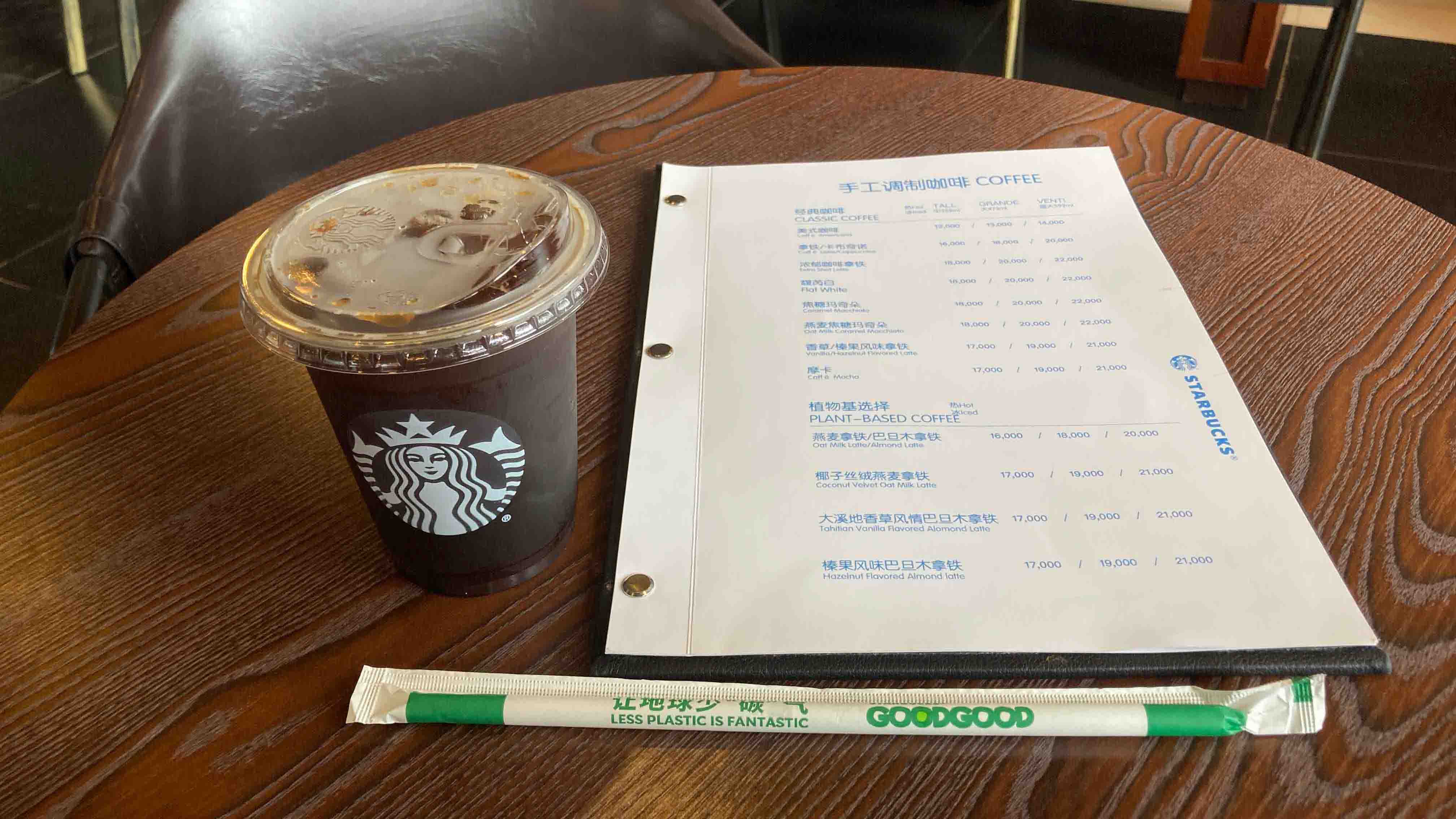 木製テーブルの上に置かれたスターバックスのアイスコーヒー、2言語のメニューと「LESS PLASTIC IS FANTASTIC」と書かれたエコストロー。