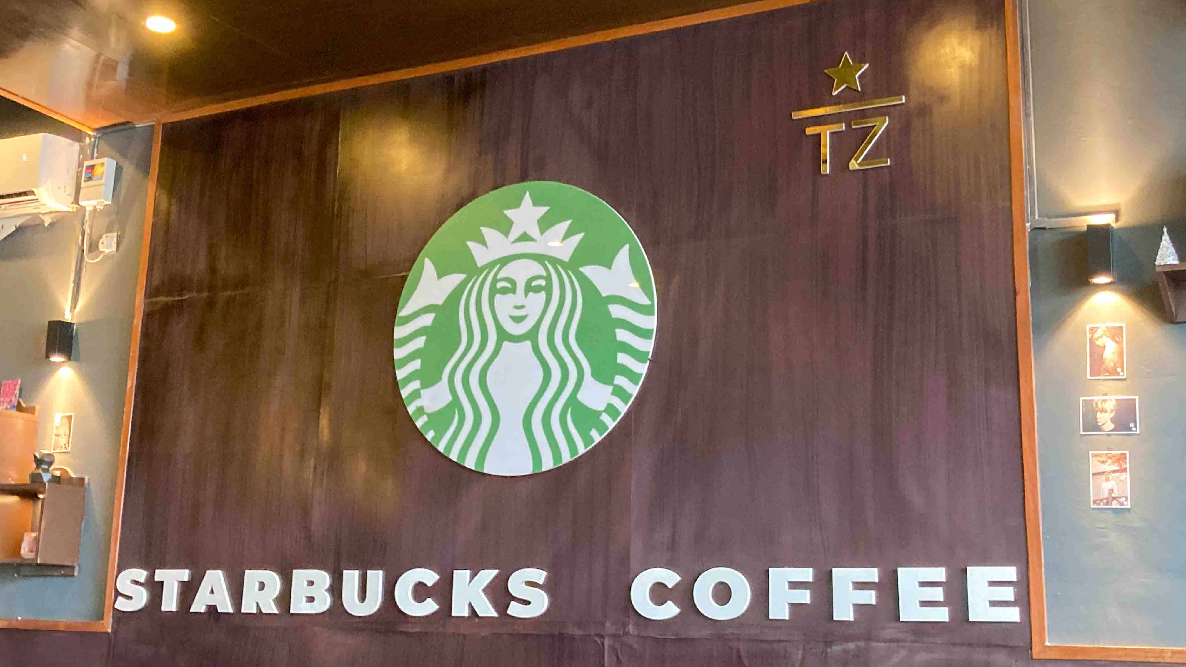 Large Starbucks logo on a wooden wall inside the store, with “TZ” initials and soft lighting.