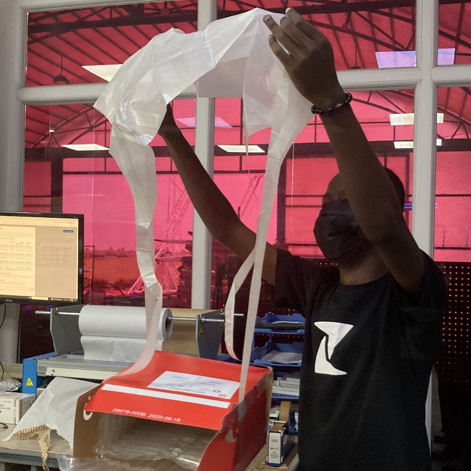 A Zipline staff member prepares a red delivery box with a parachute for aerial drop of medical supplies.