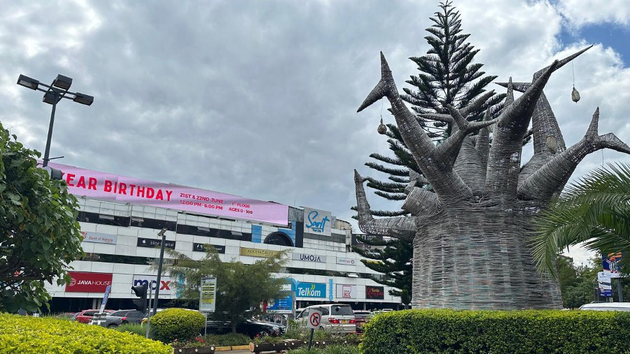 View of Sarit Centre shopping mall in Nairobi with a distinctive metal tree sculpture in the foreground.