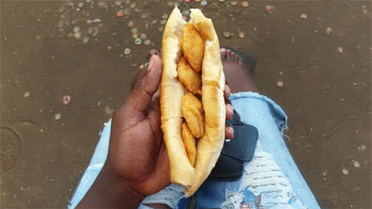 A glass bottle of coconut milk next to whole and halved coconuts on a light surface with a rustic wall in the background.