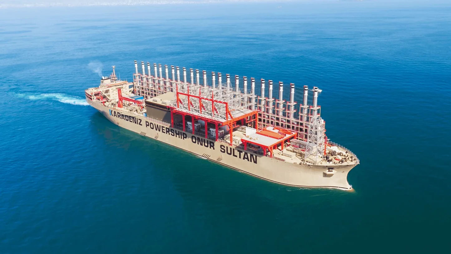 複数の排気筒と発電設備を備えた大型の海上発電船「カラデニズ・パワーシップ・オヌル・スルタン号」が、穏やかな青い海を航行している空撮画像。