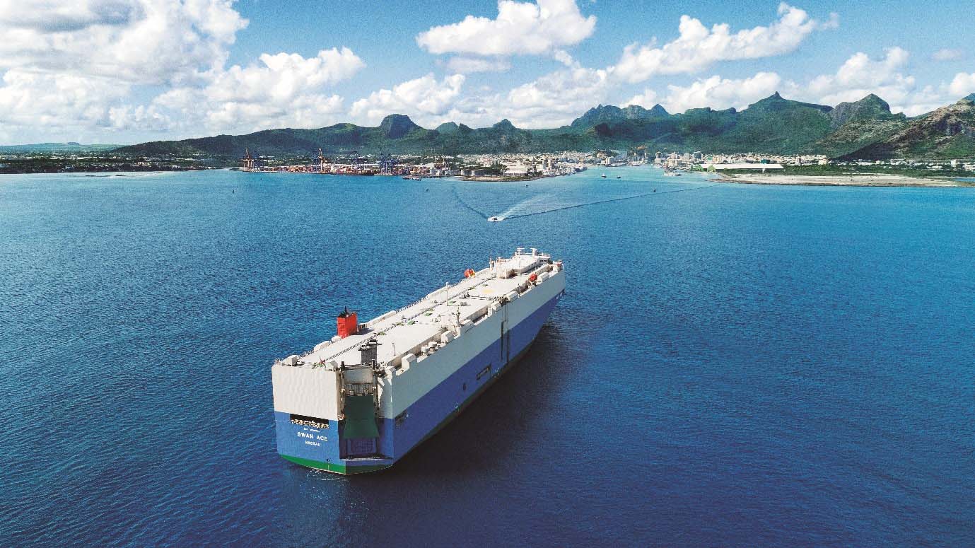 MOLの自動車運搬船「Swan Ace」がモーリシャス・ポートルイスに到着する様子。背景には山と港の風景が広がる。