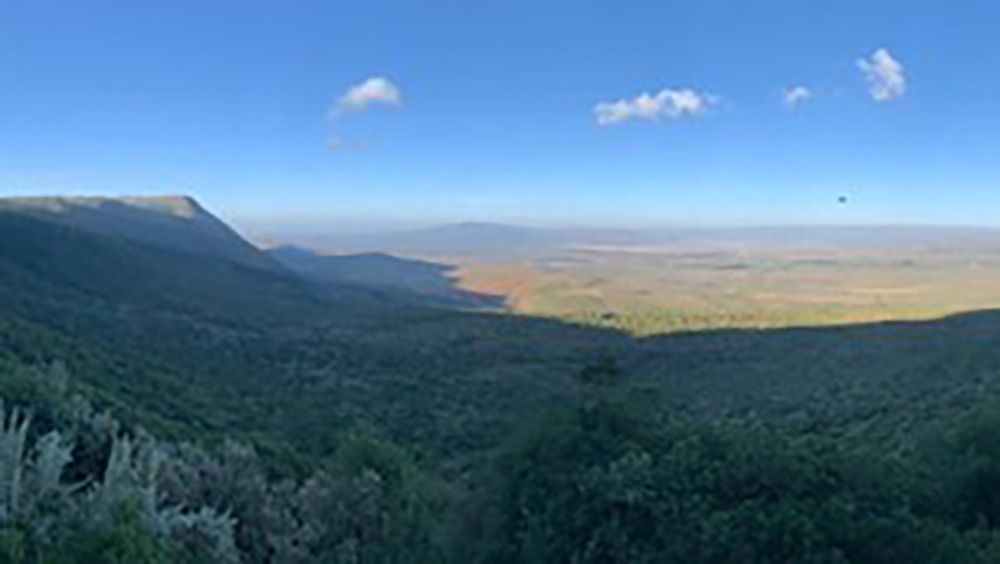 Panoramic view of the Great Rift Valley in Kenya, with lush green hills in the foreground and vast plains stretching into the distance under a clear blue sky.