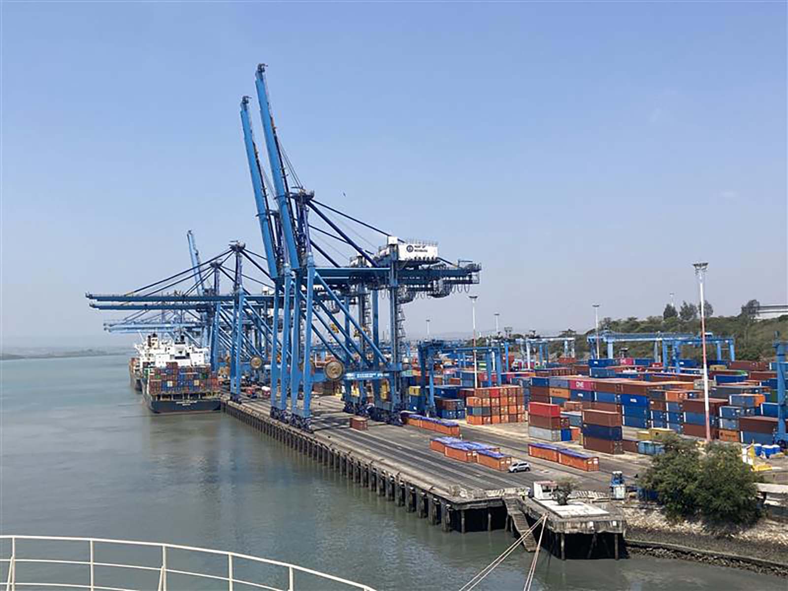 A wide view of Mombasa Port’s container terminal showing large blue gantry cranes loading and unloading cargo ships, with colorful shipping containers stacked along the quay under clear skies.