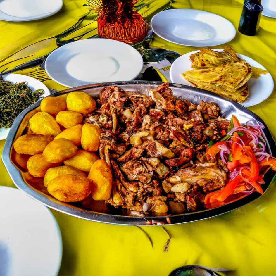 A platter with fried potatoes, grilled meat, sliced vegetables, and chapati served on a colorful table setting.