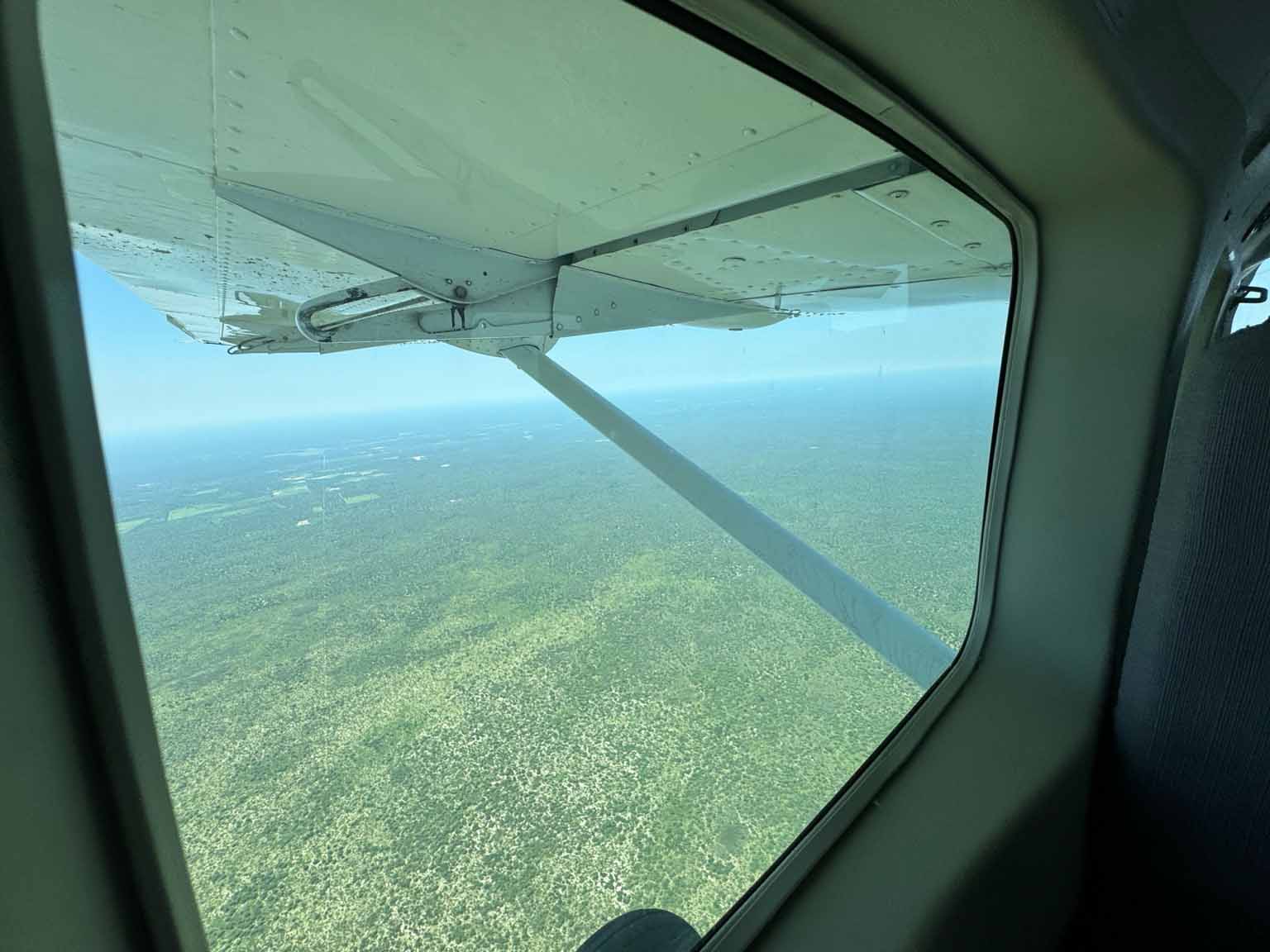 View from a small aircraft window, showing vast green landscape stretching into the distance.