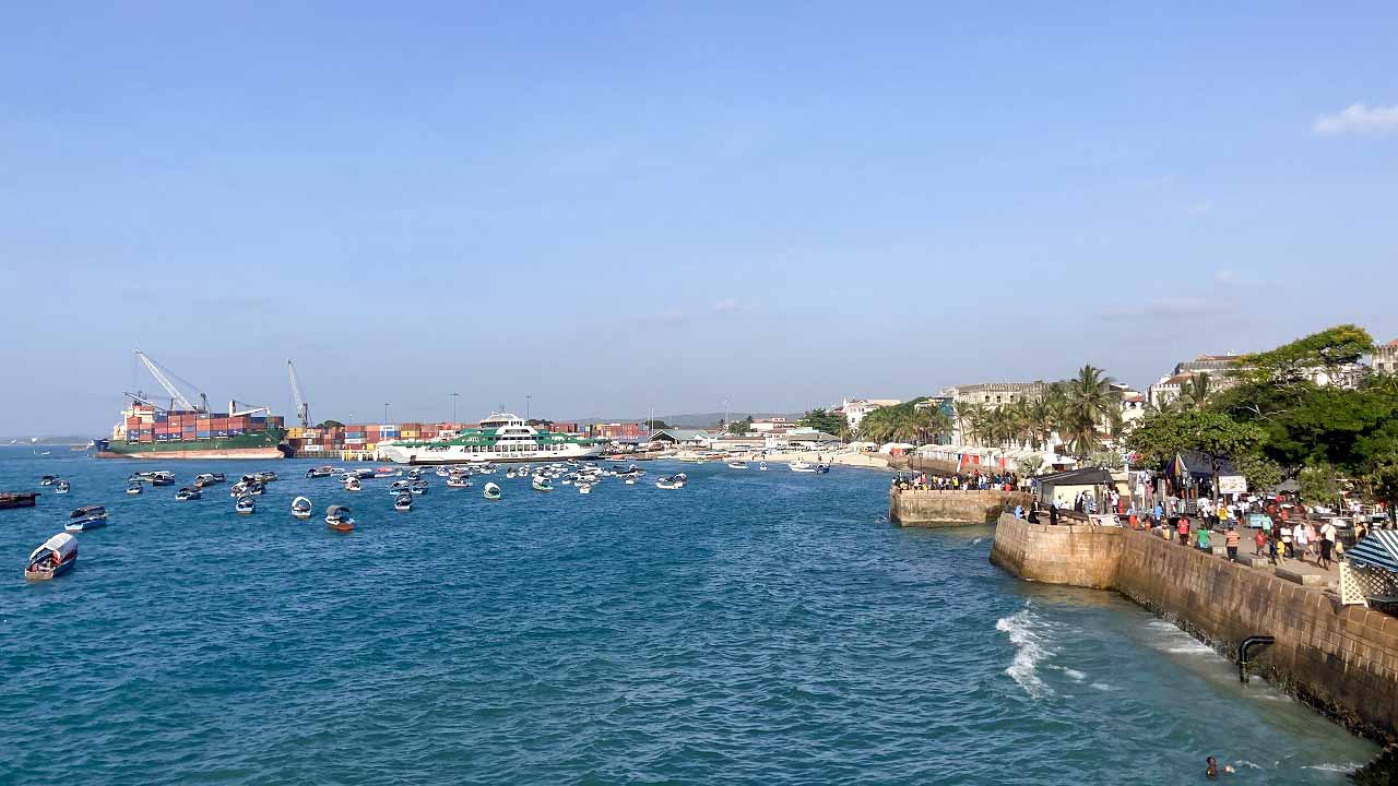 ターコイズブルーの海に小型ボートが浮かび、背景にストーンタウンの海岸線が広がるザンジバル港の風景。