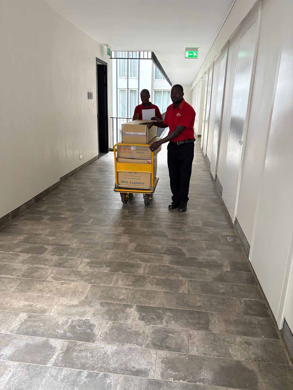 MOL Logistics staff transporting unaccompanied baggage boxes through an apartment corridor after arrival in Kenya.