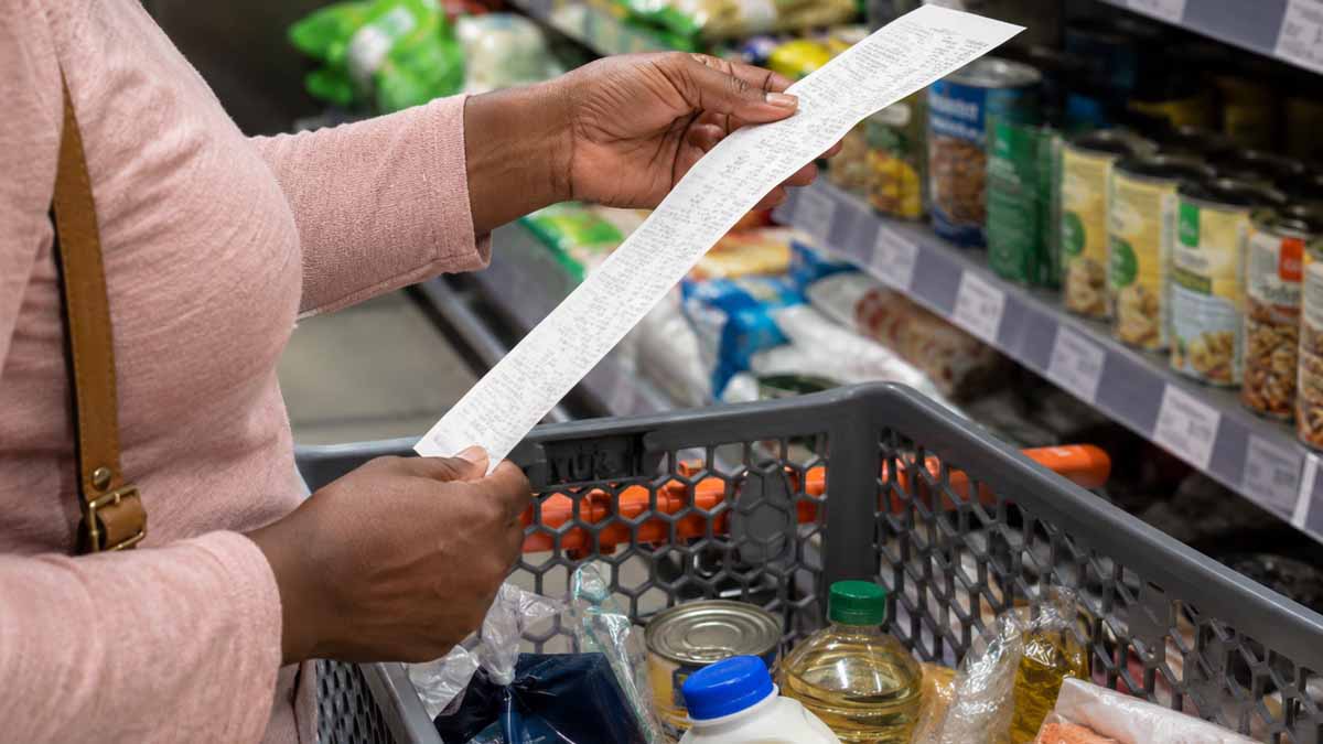 A shopper checking a long receipt in a supermarket, illustrating how higher fuel and logistics costs can gradually affect food prices and household expenses.