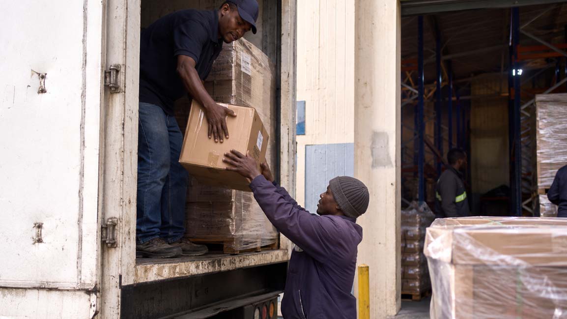 Warehouse workers unloading cargo from a truck, representing the importance of stable logistics networks and supply chains during global geopolitical disruptions.