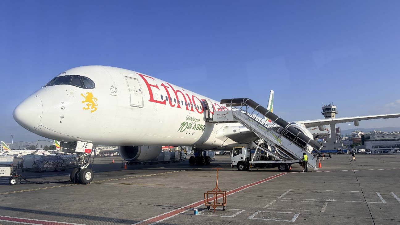 Ethiopian Airlines aircraft parked at Addis Ababa airport with passenger stairs connected under a clear blue sky.