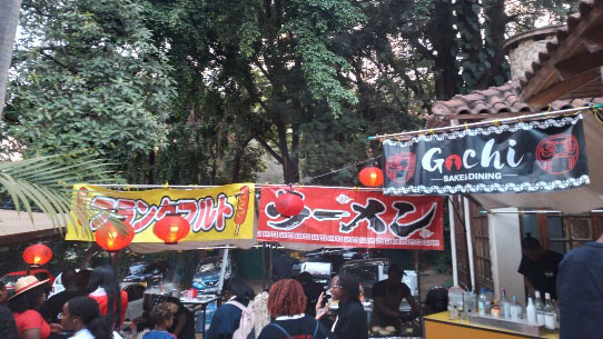 Japanese food stalls with ramen banners and red lanterns set up under trees at a cultural festival in Kenya.