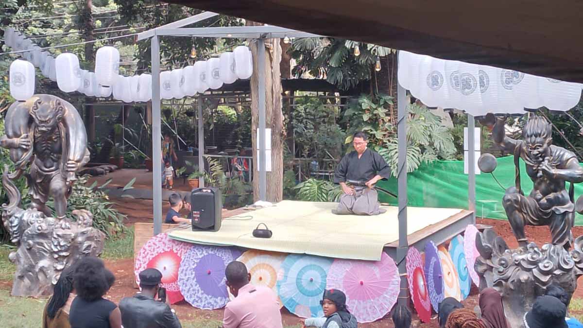 Performer seated on a tatami-style outdoor stage decorated with Japanese umbrellas, lanterns, and statues at a cultural festival in Kenya.