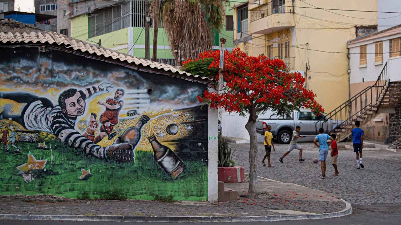 カーボベルデの住宅街で、色鮮やかな壁画のそばでサッカーをする子どもたち。