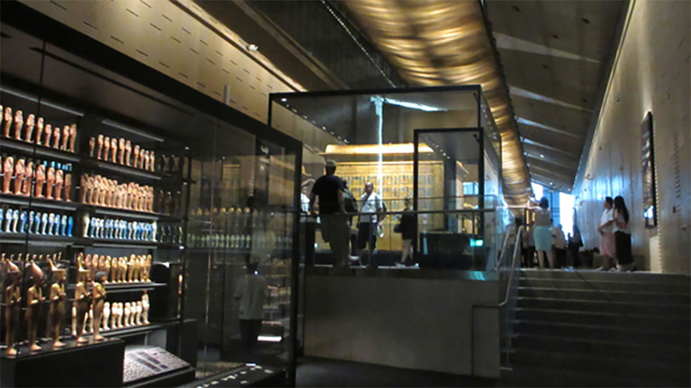 大エジプト博物館の展示室に並ぶ古代エジプトの遺物や小像。ライトアップされたガラスケースを通じて、エジプトの豊かな考古学的遺産を紹介。