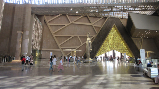 大エジプト博物館の壮大なエントランスホール。巨大な古代エジプトの石像、幾何学的な現代建築、自然光が差し込む広々とした空間が印象的。