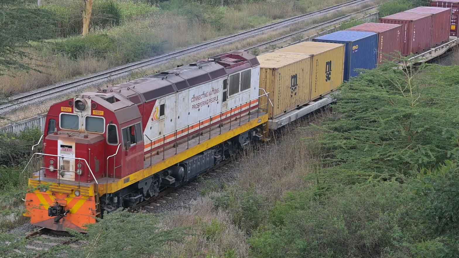 緑豊かな自然の中を走行するケニアの標準軌鉄道（SGR）の貨物列車。ディーゼル機関車がコンテナを積載した貨車を牽引している。