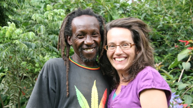 A smiling man and woman standing together in a lush green garden, surrounded by tropical plants at Mlango Farm in Kenya.