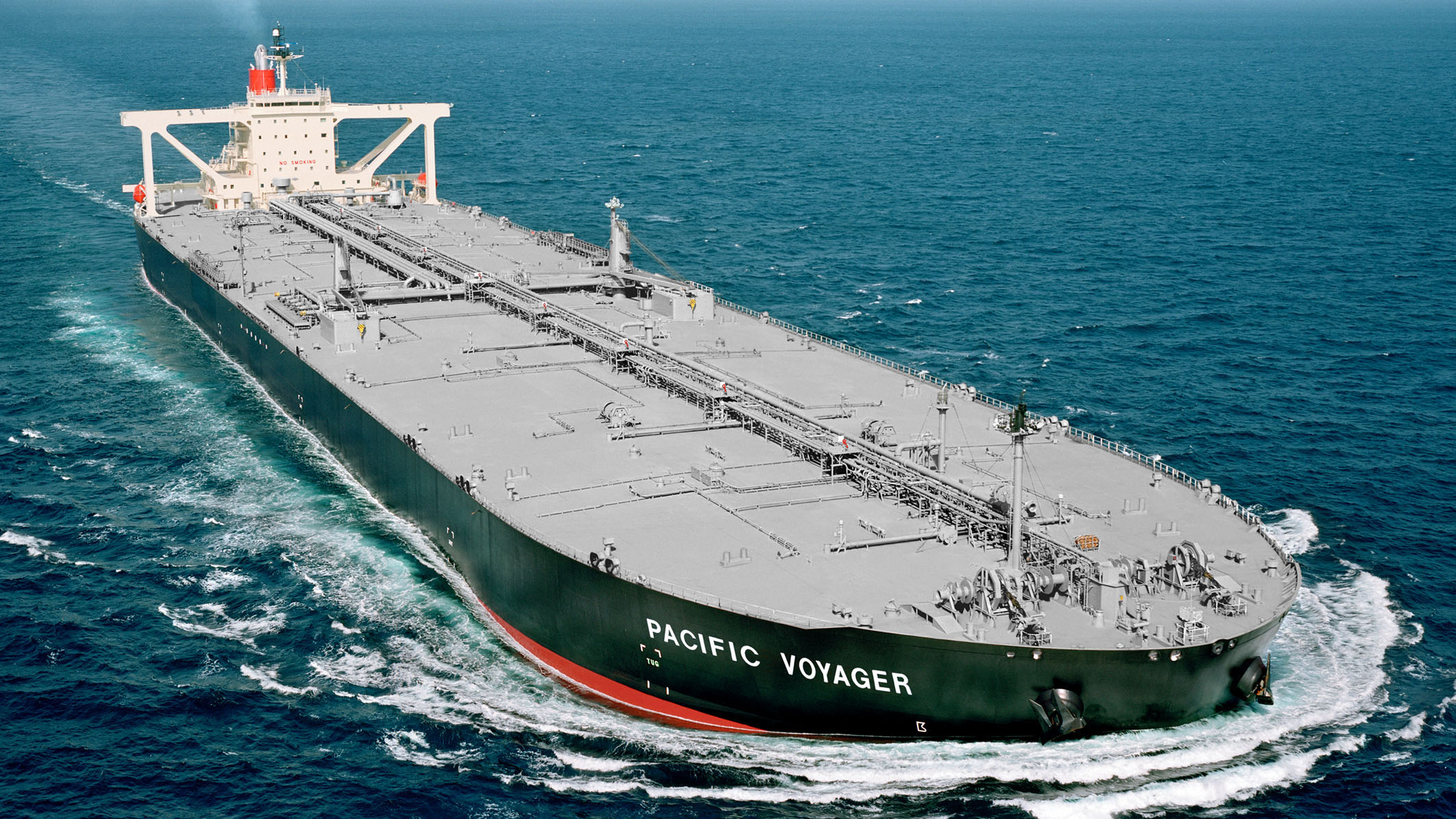 A large red tanker named ‘Pacific Voyager’ sails through rough seas, cutting through the waves with its bow, showcasing the vessel’s robust capabilities.