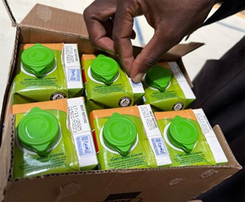 ケニアの倉庫で、緑のキャップが付いた飲料パックを箱から取り出す様子。