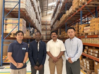 物流倉庫内で、スタッフと現地スタッフが並んで記念撮影している様子。